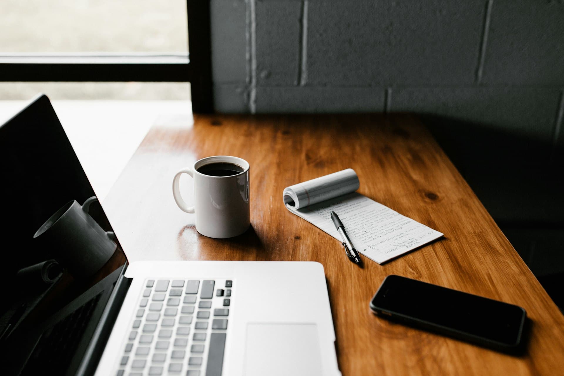 Laptop and notebook on a quiet desk beside a window